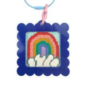 Needlepoint rainbow design in a blue frame with a pink clip on a white background bag tag