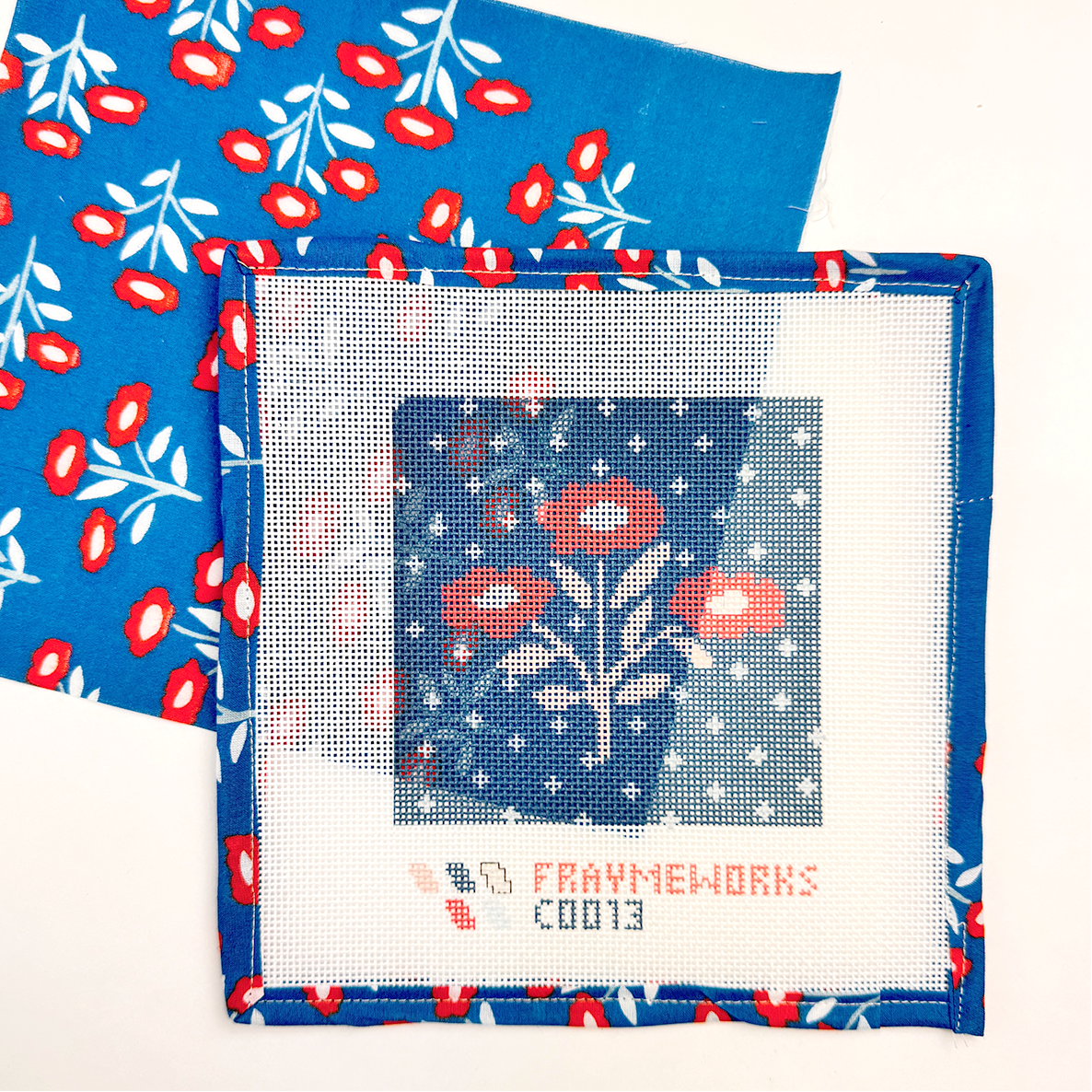 Needlepoint canvas kit with floral design  by and blue fabric with red and white pattern. Pattern is Juliet from Handker