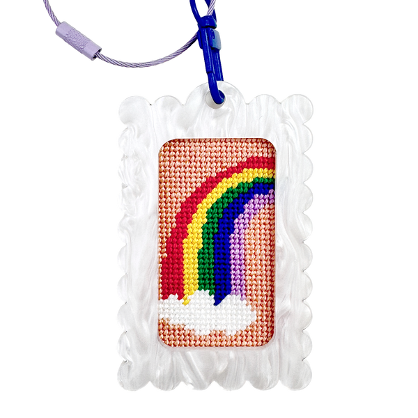 Needlepoint rainbow design in a bag tag keychain white frame with a blue clip against a white background