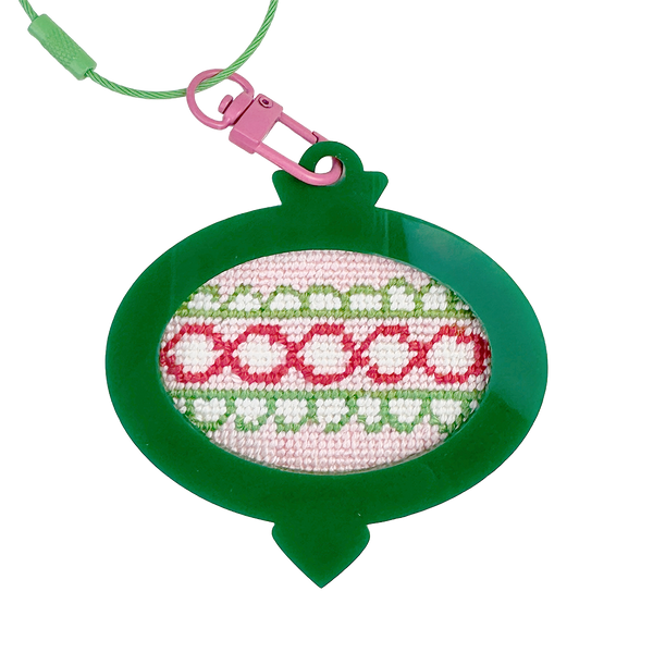 Needlepoint Christmas ornament design in a green frame with pink and white pattern on a white background