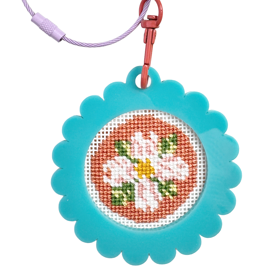Cross-stitched bag tag keychain with floral design on a blue frame, attached to a metal clip and wire