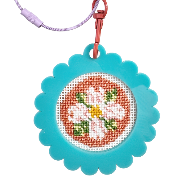 Cross-stitched bag tag keychain with floral design on a blue frame, attached to a metal clip and wire